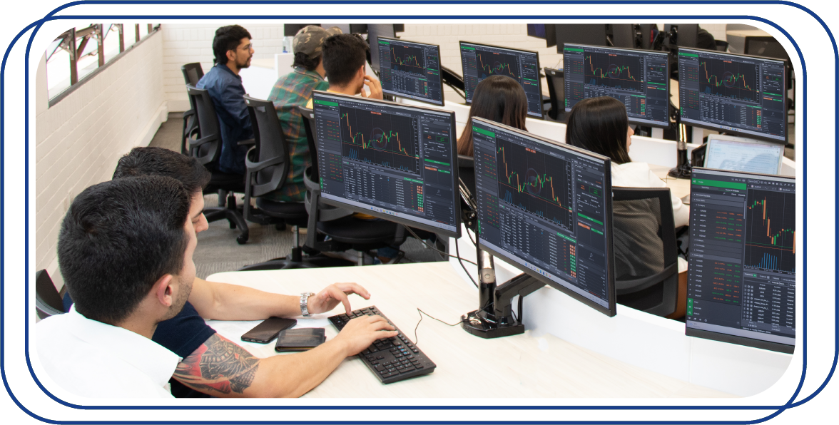 Personas sentadas frente a un computador con imágenes relacionadas a la bolsa de valores
