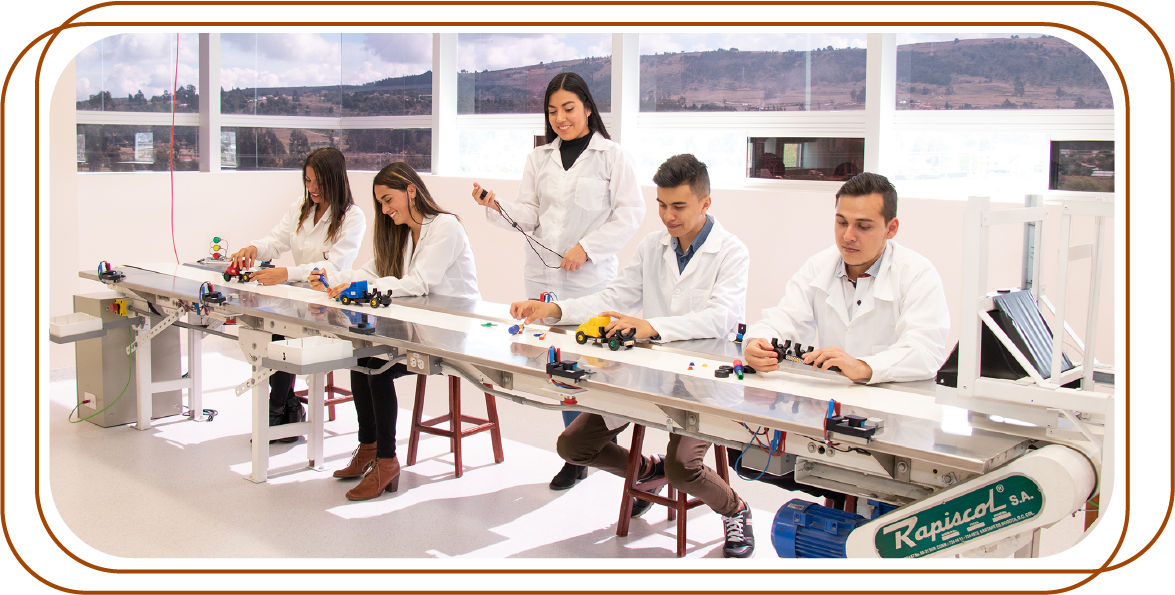 La imagen muestra a un grupo de personas sentadas en una larga mesa en un entorno de laboratorio. Están trabajando con diversas herramientas y componentes electrónicos,