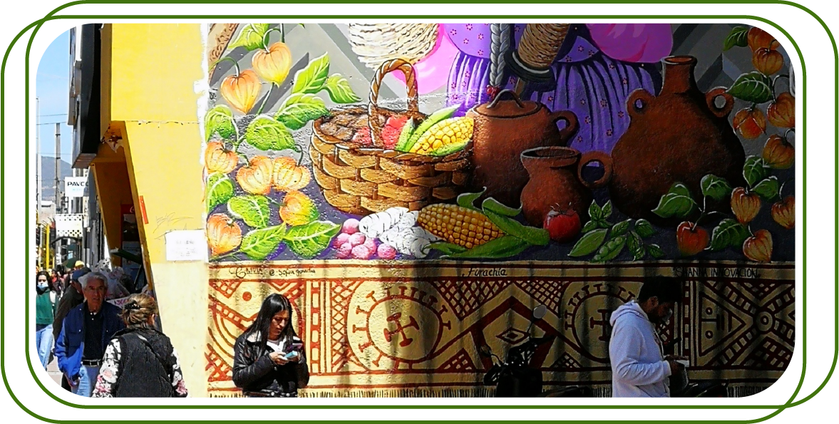  mural colorido en una pared que representa una escena con elementos de la cultura y gastronomía tradicional. En el mural, se pueden ver una canasta con vegetales y frutas, varias ollas de barro y una mujer con una vestimenta típica. En la parte inferior del mural, hay un patrón decorativo de estilo indígena. La escena está en un entorno urbano, con personas caminando y una fachada amarilla a la izquierda.